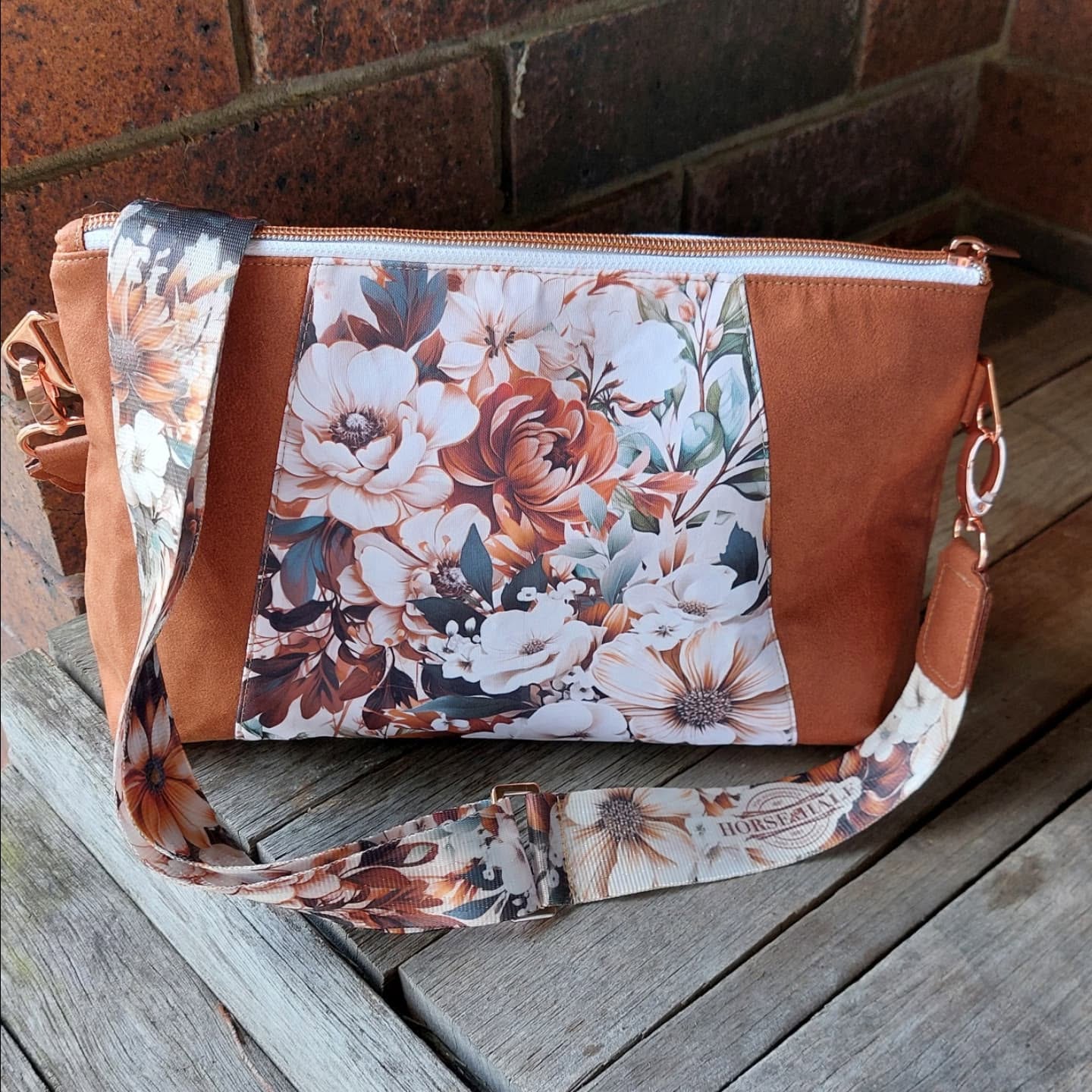 Brown handbag with floral strap on a wooden surface